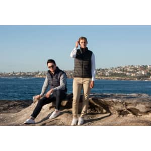 A puffer vest in black, worn by two models by the seaside, with a scenic coastal background.