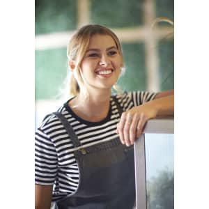 A smiling woman in a striped t-shirt and overalls leans against a display, surrounded by greenery.