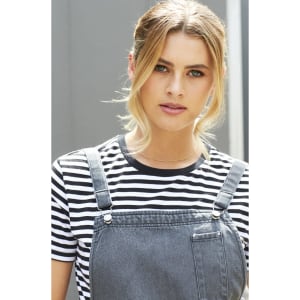 A model wearing a grey bib apron over a black and white striped shirt, featuring a front pocket and adjustable straps.