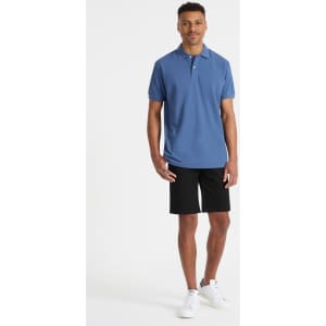 A men's polo shirt in blue, paired with black shorts, displayed on a model. The shirt features a logo.