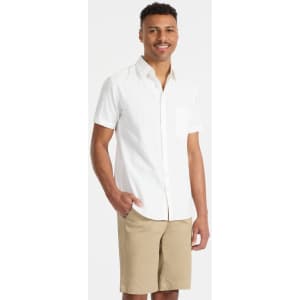 A short-sleeve white button-up shirt with a chest pocket, modelled by a smiling man wearing beige shorts.