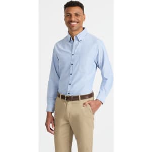 A light blue button-up shirt with long sleeves and a chest pocket, paired with beige trousers. The model is smiling and standing.