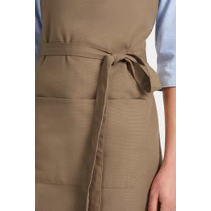 A khaki bib apron featuring a tied waist and a front pocket, with a light blue shirt visible underneath.