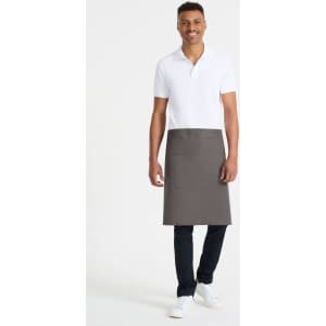 A waist apron in dark grey, featuring a front pocket, worn by a model in a white polo and black pants.