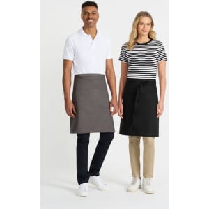 A couple of models stand side by side, one in a black and white striped t-shirt and the other in a white polo, both wearing aprons.