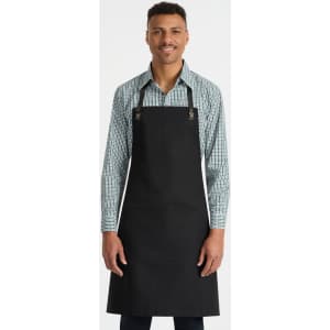 A black bib apron with adjustable straps, featuring a front pocket, worn by a model in a checkered shirt.