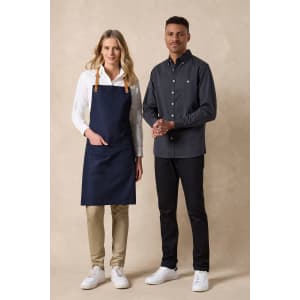 A man in a dark button-up shirt and a woman in a white blouse with a navy apron, both wearing casual shoes.