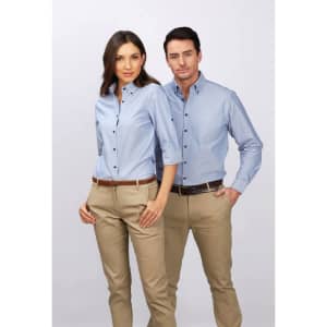 A light blue button-up shirt worn by a man and a woman, both styled with beige trousers. The shirt features a logo.