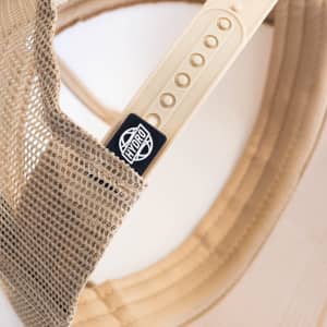 A beige cap featuring a mesh back and a logo on the side, highlighting its headwear design.