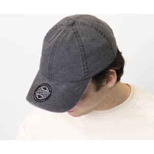 A grey 6-panel chino cotton twill cap featuring a front logo, worn by a person with their head down.