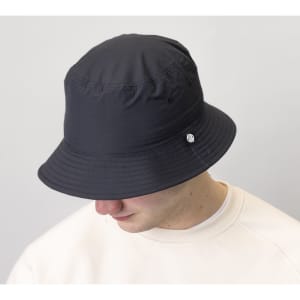 A black chino cotton twill bucket hat featuring a small logo, worn by a person with a neutral background.