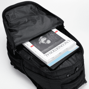 A black backpack with a partially open zipper, revealing magazines and documents inside. It features a logo on the exterior.