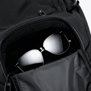 A black backpack with a zippered pocket containing a pair of dark sunglasses inside.