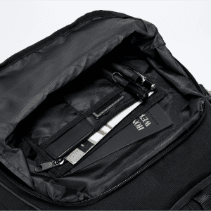 An open black backpack interior featuring a pen, a cardholder, and a small notebook.
