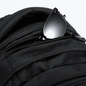 A black backpack featuring multiple zippered pockets and a pair of black sunglasses resting in one of the pockets.