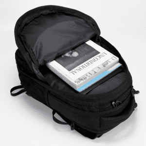 A black Fitzroy Backpack open, revealing stacked magazines and a notebook inside. The bag has a sleek design and features.