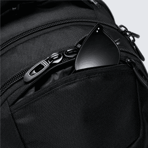 A black backpack with a textured finish and a small black item peeking from a front zippered pocket.