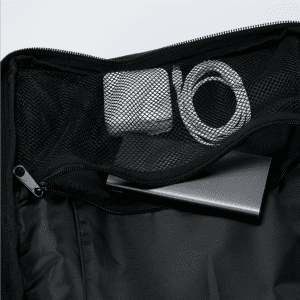 A black Eiger backpack interior featuring a metal device, tape, and a charging cable inside a mesh pocket.