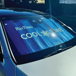 A foldable car sunshade in blue with branding, placed on the windshield of a silver car.
