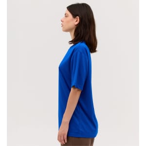 A blue short-sleeve tee is displayed on a model from a side view, featuring a simple design and a comfortable fit.