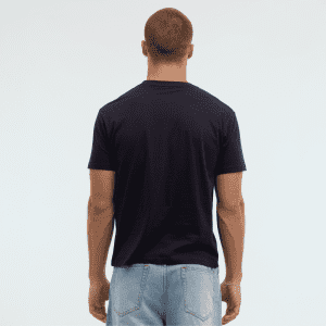 A navy Essential/Surf Tee displayed from the back on a model, wearing light blue jeans. The tee has a logo.