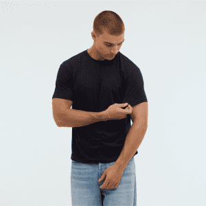 A man wearing a navy blue Essential/Surf Tee and light blue jeans, looking at his sleeve. The image features a logo.