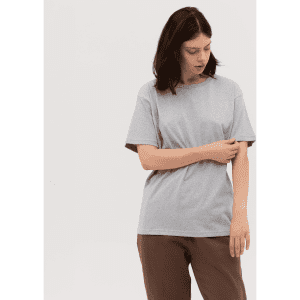 A grey t-shirt is displayed on a model, styled with loose-fitting brown trousers. The model has dark hair and a neutral expression.