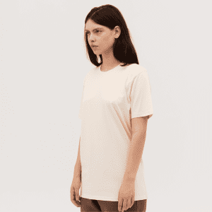 A plain light peach Classic Tee displayed on a model standing against a neutral background. The tee has a simple design and a logo.