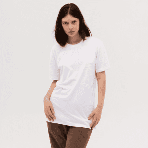 A woman wearing a plain white T-shirt, styled with brown trousers, posing against a neutral background.