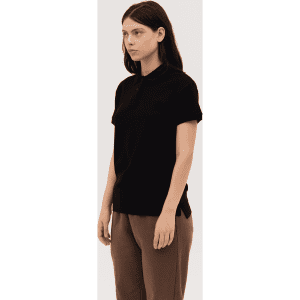 A black women's polo shirt with a classic collar and short sleeves. The model is standing in a neutral pose.