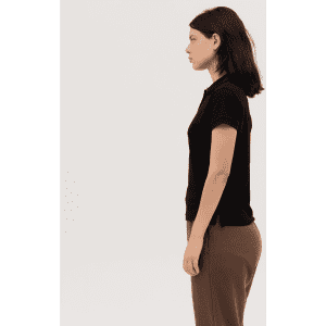 A black women's polo shirt is displayed on a model, shown in profile. The design includes short sleeves and a fitted shape.