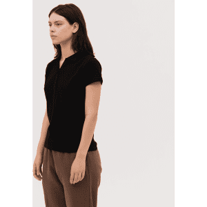 A black women's polo shirt with a zip front and short sleeves, paired with light brown trousers.