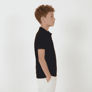 A side view of a youth wearing a black polo shirt paired with white trousers. The shirt has a branded logo.