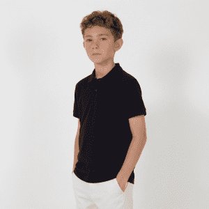 A youth black polo shirt with a collar, featuring short sleeves and a pocket. The model is standing with hands in pockets.
