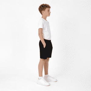 A pair of black youth shorts featured on a child wearing a white t-shirt and white shoes, standing in profile.