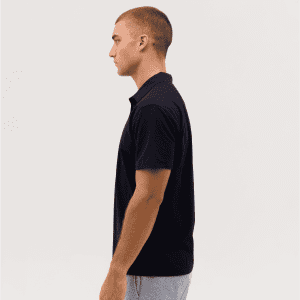 A side view of a black polo shirt on a model, featuring a collar and short sleeves. The shirt has a logo.