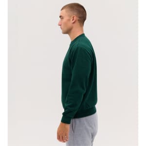 A green crew sweatshirt worn by a male model, paired with grey sweatpants, displayed from the side.