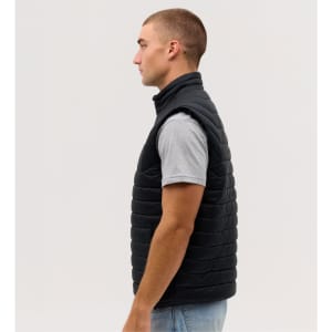 A man in a side profile wearing a black puffer vest over a grey t-shirt. The vest has a logo on it.