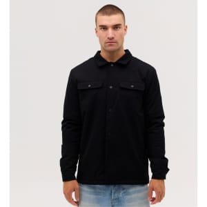 A black Studio Canvas Jacket features a collared design and front pockets, worn by a model against a plain background.
