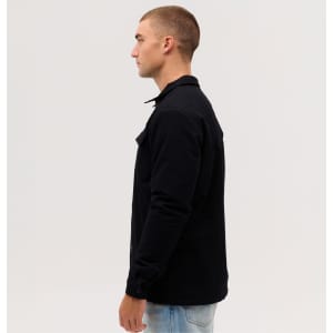 A man models a black Studio Canvas Jacket from the side, featuring a collared design and two front pockets.
