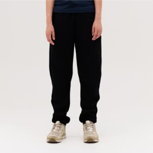 Black track pants with a relaxed fit, paired with beige shoes. The model stands against a plain background.