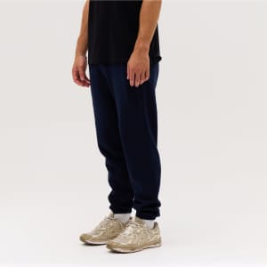 Navy track pants displayed on a person, paired with light-coloured sneakers, set against a neutral background.