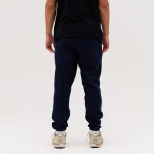 Navy blue track pants are displayed, featuring a casual fit and elastic cuffs, paired with a black shirt and light sneakers.