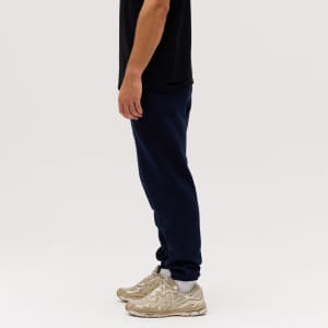 Navy track pants featured on a person, paired with beige sneakers, against a plain white background.