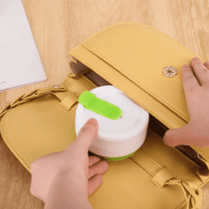 A collapsible silicone cup in white and green being placed into a yellow bag, with a hand holding it.