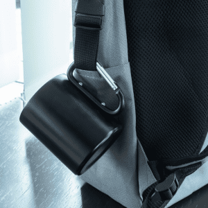 A black thermo mug attached to a grey backpack with a carabiner clip.
