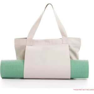 A canvas bag in light grey with two handles, holding a green yoga mat. The bag features a logo on it.