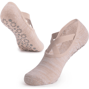 A pair of beige yoga socks featuring a cross-strap design and a textured grip sole.