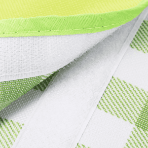 A green and white checkered picnic blanket with a textured surface and a soft lining along the edge, featuring a logo.
