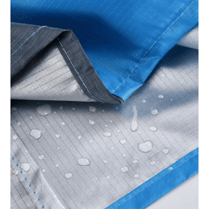 A close-up of a blue polyester picnic blanket featuring a water-resistant underside with droplets. It has a logo.